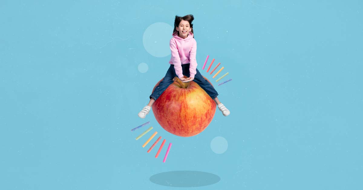 Young girl playfully jumping on an oversized apple